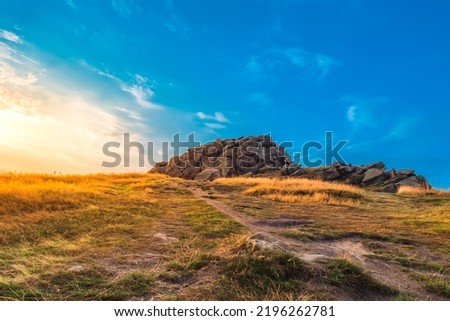 Beautiful sunrise over Almscliffe Crag, North Yorkshire. Bright, golden light shines upon the grass surrounding the millstone grit outcrop rock formation.