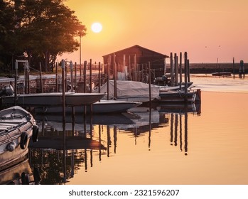 Beautiful sunrise over fishing pier ; boathouse, boats and pier reflected in calm water - Powered by Shutterstock