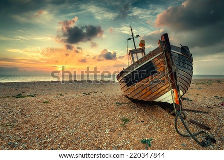 Beautiful sunrise over an old wooden fishing boat on a pebble beach, vintage effect.