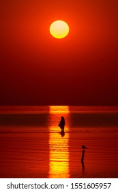 Beautiful Sunrise Over Water And Silhouette Of Old Woman Fishing