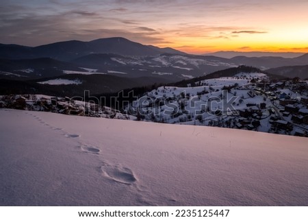 Beautiful sunrise view with snowy mountain slopes and small village among them in the frozen winter morning, the Rhodopi Mountains, Bulgaria