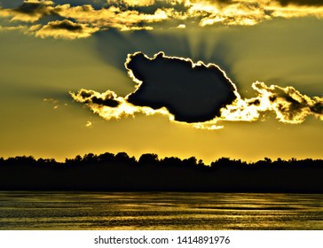 Beautiful Sunset With Big Dark Cloud Blocking The Sun, Beams Of Light Above Water In Florida's Everglades With A Silhouette Of Trees Beneath