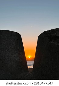 Beautiful sunset framed between two large concrete breakwater blocks on the beach at dusk