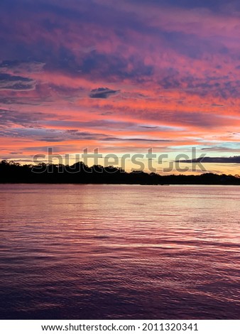Beautiful sunset on Amazon river. Peru. Amazonia. Colorful fantastic cloudy sky in summer. Before the rain in evening. Nature landscape. Scenery background. No filter. Vertical image.