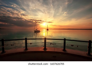 Beautiful sunset on Lake Balaton with two sailboats, with Siófok pier in the foreground. Colorful summer background from the hungarian see. - Powered by Shutterstock