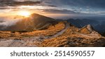 Beautiful sunset on mountain with trail leading up side. Trail is surrounded by grass and rocks. Sun is setting behind mountain, casting warm glow on landscape