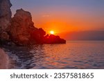 Beautiful sunset on the sea coast. Rocky coast of the sea, the leaving bright sun behind the mountain.