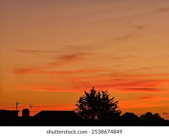 A beautiful sunset with orange and pink hues paints the sky above a quiet neighborhood. Silhouetted rooftops and trees add contrast to the vibrant colors, creating a tranquil evening scene - Powered by Shutterstock