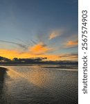 Beautiful sunset  with orange, yellow, and pink hues mirrored onto clear tranquil water with puffy clouds in New Zelanad beach 