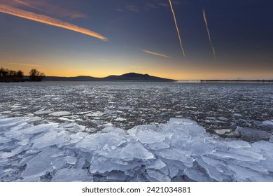 Beautiful sunset over the Pálava Hills. In the foreground, white ice floe lying on the shore of the lake.