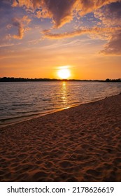 Beautiful Sunset Over The River (lake, Pond). Beach And Sand. The Sun Goes Below The Horizon. Clouds In The Sky. Orange And Blue Colors