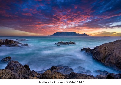 Beautiful sunset sky above a wispy long-exposure sea. Table Mountain sets the backdrop for a vibrant and colourful panorama