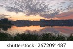 Beautiful sunset sky with dramatic clouds over calm river reflecting city skyline and green grass in the foreground.