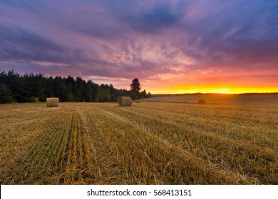 Beautiful sunset sky over stubble field and straw bales. European countryside.