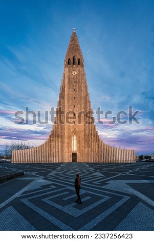 Beautiful sunset sky shining on Hallgrimskirkja Lutheran parish church is the largest church in centre and female tourist standing at Reykjavik downtown, Iceland