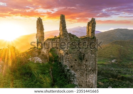 beautiful sunset or sunrise landscape of ancient ruins on a top of a hill with green mountains with white snow top on background