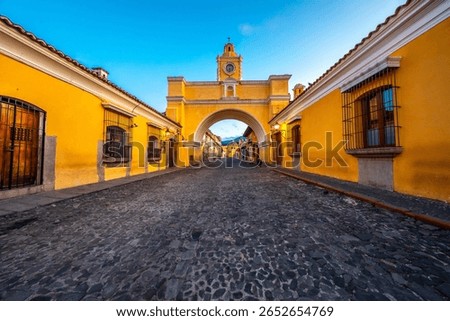 A beautiful sunset view down a cobblestone street in Antigua Guatemala, featuring the iconic Santa Catalina Arch and volcanic backdrop.