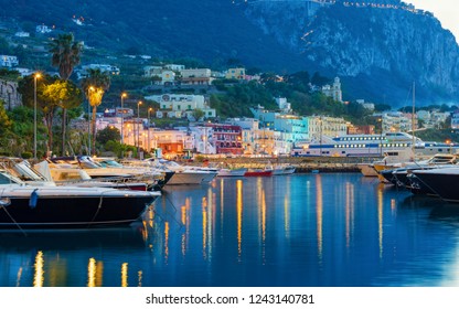 Beautiful Sunset View Of Marina Grande, Capri Island, Italy. Illuminated Streets Of City Are Reflected In Serene Sea. Photo Taken Witn Long Exposure.