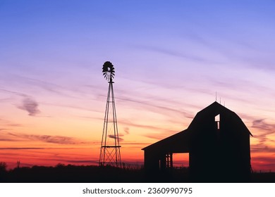 A beautiful sunset of a windmill and barn silhouetted against the evening sky in rural Indiana USA, North America