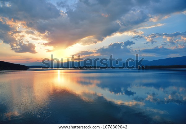 Beautiful Sunset. Sun, lake. Sunrise Landscape. Beauty in Nature themed wallpaper. Blue Sky. Amazing Colorful Clouds. Water Reflections .Magic Artistic Wallpaper. Creative Orange Background. Tranquil Natural Art Photography.