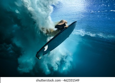 Beautiful Surfer Diving Duckdive under Big Ocean Wave. Turbulent air bubbles and tracks after sea wave crashing. Ripples at water surface with sky color. - Powered by Shutterstock