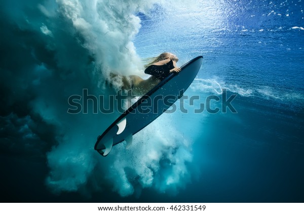 Beautiful Surfer Diving Duckdive under Big\
Ocean Wave. Turbulent air bubbles and tracks after sea wave\
crashing. Ripples at water surface with sky\
color.