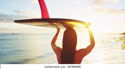 Beautiful surfer girl walking down the beach into the sunset