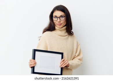 A Beautiful, Sweet, Attractive Woman In Black Glasses For Vision, With Long Dark Hair, With Empty White Frame In Her Hands. Studio Photography With Space For Advertising Mockup