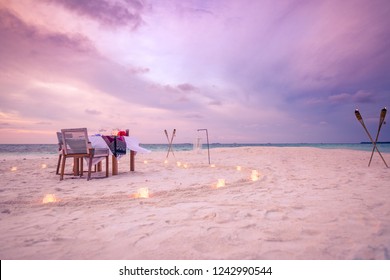 Beautiful Table Set Up For A Romantic Meal On The Beach With Lanterns And Chairs And Flowers With Candles And Sky And Sea In The Background. Sunset Beach Dinner