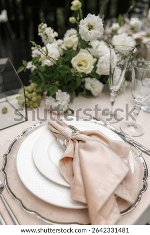  Beautiful table setting featuring white plates, a blush napkin with a glass holder, and polished silver cutlery. Glasses are neatly arranged, creating a sophisticated dining atmosphere.