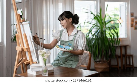 A beautiful and talented young Asian female artist painting on a canvas with water colors, working in her cosy minimalist studio alone. Creativity and inspiration concepts - Powered by Shutterstock