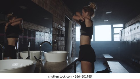 Beautiful Tall Sporty Blonde Woman Washing Face, Looking In The Mirror In Dark Gym Locker Room Exhausted Slow Motion.