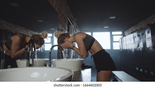 Beautiful Tall Sporty Blonde Woman Washing Face, Looking In The Mirror In Dark Gym Locker Room Exhausted Slow Motion.