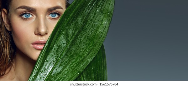 Beautiful Tanned Blue-eyed Girl With Natural Make-up And Wet Hair Holds Wet Exotic Leaves Near Her Face.Beauty, Fashion, Cosmetology, Natural, Nature, Natural, Spa, Detox, Plants.