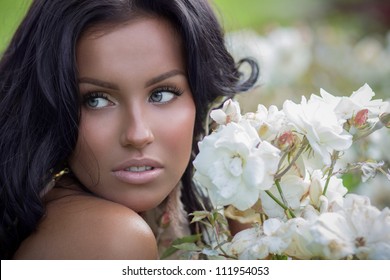Beautiful tanned brunette posing near white roses