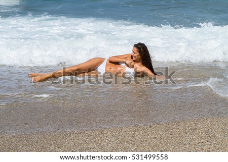 Beautiful tanned brunette in white bikini lying on the beach