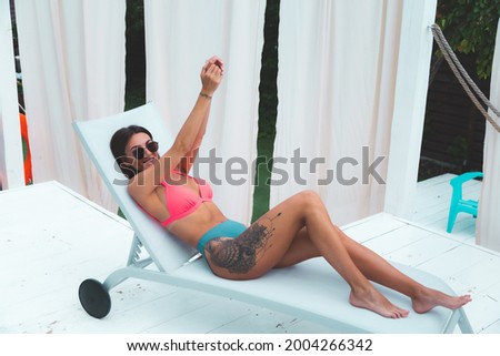 Beautiful tanned fit woman in bikini in backyard posing outdoor by pool on sunbed