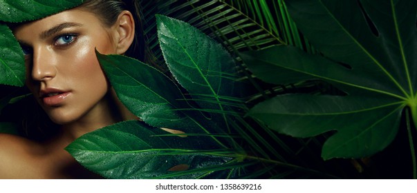 A beautiful tanned girl with natural make-up and wet hair stands in the jungle among exotic plants.