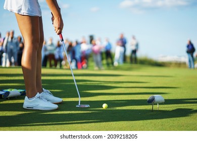 Beautiful tanned legs of a golfer girl on the golf course. Girl player with golf clubs on the lawn prepares to hit. Sports and summer hobbies. - Powered by Shutterstock