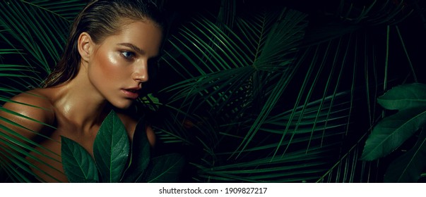 A beautiful tanned young woman with natural makeup and wet hair stands in the jungle among exotic plants. Tropical plants, nature
