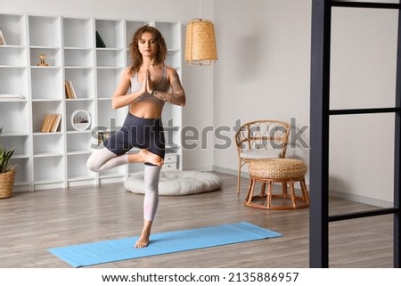 Beautiful tattooed young woman practicing yoga at home