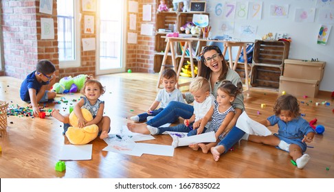 Beautiful teacher and group of toddlers sitting on the floor drawing using paper and pencil around lots of toys at kindergarten - Shutterstock ID 1667835022
