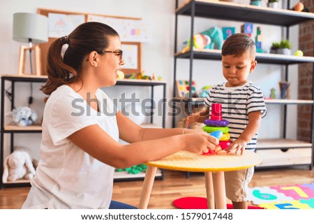 Beautiful teacher and toddler boy building pyramid with hoops bolcks at kindergarten