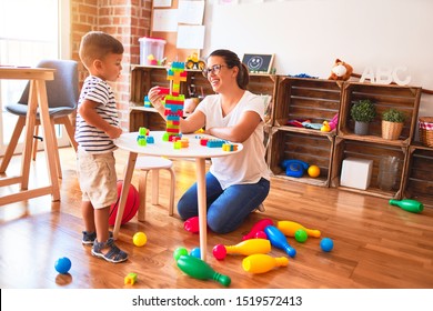 Beautiful teacher and toddler boy playing with construction blocks bulding tower at kindergarten