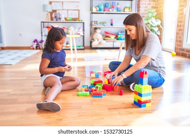 Beautiful teacher and toddler girl playing with construction blocks bulding tower at kindergarten - Shutterstock ID 1532730125