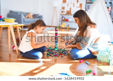 Beautiful teacher and toddler playing with building blocks toy around lots of toys at kindergarten