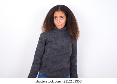 beautiful teen girl with afro hairstyle wearing grey turtleneck sweater against white making grimace and crazy face, screaming out of control, funny lunatic expressing freedom and wild.