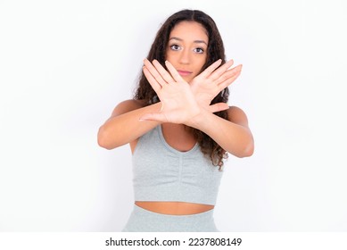 Beautiful teen girl with curly hair wearing grey sport set over white background has rejection expression crossing arms and palms doing negative sign, angry face. - Shutterstock ID 2237808149