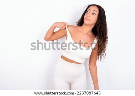 Beautiful teen girl with curly hair wearing white sport set over white background stressed, anxious, tired and frustrated, pulling shirt neck, looking frustrated with problem