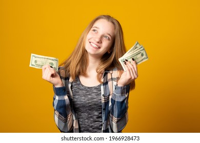 Beautiful Teen Girl Holding Dollars. Happy Girl Holding Money Banknotes And Celebrating On Yellow Background.